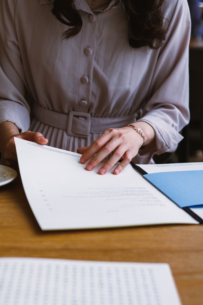A woman in elegant attire reviews important documents at a wooden desk, focused and professional.